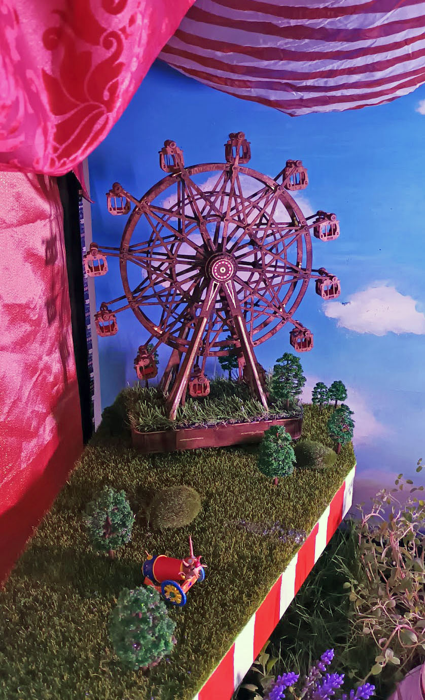 The circus Ferris wheel in front of a red curtain backdrop, ringed with living greenery