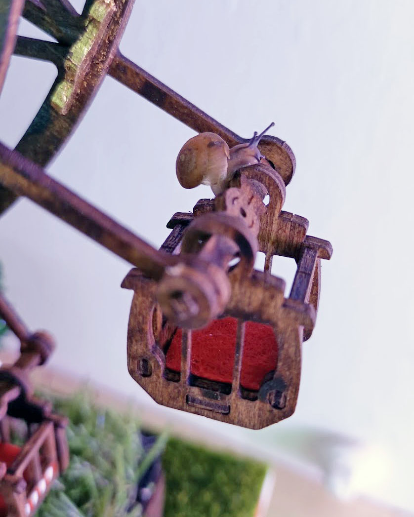 A snail riding in a tiny Ferris-wheel gondola